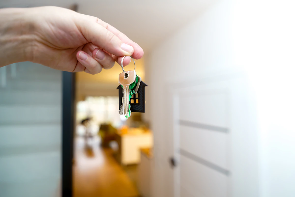 Hand holding house keys in front of an Ontario home, the goal of becoming a licensed realtor